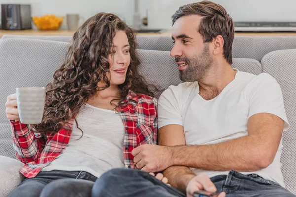 Amor verdadero. Alegre pareja romántica sentada en el sofá en una acogedora habitación y sonriendo . —  Fotos de Stock