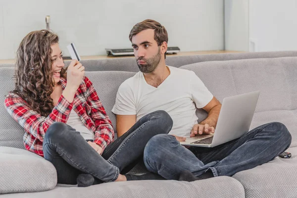 Porträt eines lachenden jungen Paares, das online einkauft, während es mit Kreditkarte und Laptop auf einer Couch sitzt. — Stockfoto