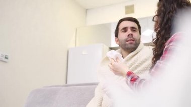 Soğuk battaniye sosisli bir kanepede oturan bir adam. Sıcaklık kontrol. Karısı onun yanında oturuyor ve yardımcı olur. Adam evde. Hasta genç odasında gri kanepe adam. Mutsuz adam. Kavramı