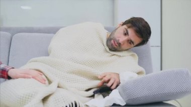 Soğuk battaniye sosisli bir kanepede oturan bir adam. Sıcaklık kontrol. Karısı onun yanında oturuyor ve yardımcı olur. Adam evde. Hasta genç odasında gri kanepe adam. Mutsuz adam. Kavramı