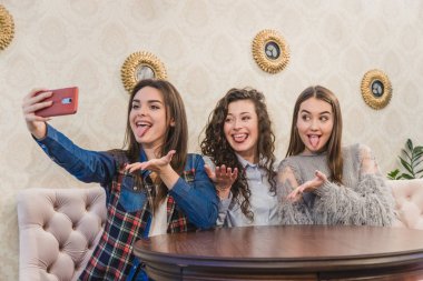 Kafede birlikte otururken, üç mutlu kız arkadaş otoportre alarak portresi. Sevimli kızlar kahve içiyor.