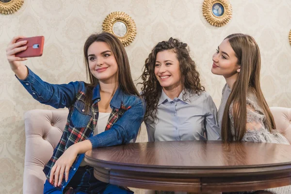 Retrato de três namoradas felizes tomando auto-retrato, enquanto sentados juntos no café. Meninas encantadoras beber café e comer bolos, sorrindo e se divertindo na reunião. Conceito de amizade . — Fotografia de Stock