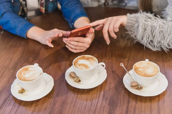 Three cups of cappuccino. Hold hands with a phone on a brown table. — Stock Photo, Image