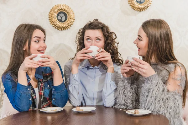 Three women friends enjoy coffee in the cafe. Enjoy coffee while chatting in the cafe. Young and beautiful girls with long blackheads. — Stock Photo, Image