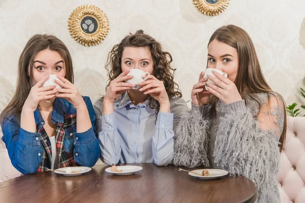Tři kamarádi si v kavárně užívají kávu. Při chatování v kavárně si vychutnejte kávu. Mladé a krásné dívky s dlouhými blackheada. — Stock fotografie