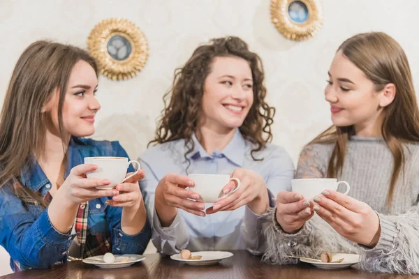 Three women friends enjoy coffee in the cafe. Enjoy coffee while chatting in the cafe. Young and beautiful girls with long blackheads. — Stock Photo, Image