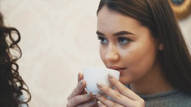 3人の若い女の子が喫茶店に座って話をする。この間、カプチーノをお楽しみください。一緒に時間を過ごすことを幸せに. — ストック動画