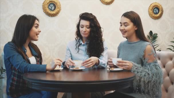 Tři mladé dívky sedí v kavárně a mluví. Během této doby si užívejte cappuccino. Rád trávíme čas spolu. — Stock video