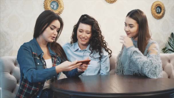 Las tres chicas jóvenes buenas están sentadas en un café y pasan tiempo comunicándose — Vídeos de Stock