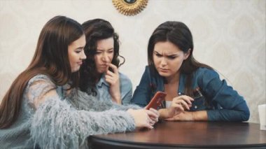 Üç arkadaş, bir kafede akıllı telefon kullanarak oturan ve komik bir konuşma yapıyor. Uzun güzel siyah saçlı iyi kızlar.