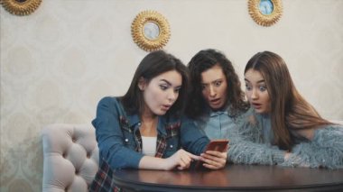 Üç arkadaş, bir kafede akıllı telefon kullanarak oturan ve komik bir konuşma yapıyor. Uzun güzel siyah saçlı iyi kızlar.