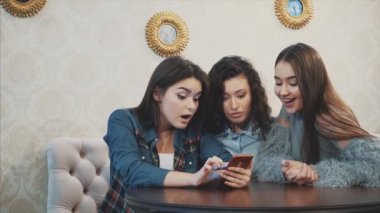 Üç arkadaş, bir kafede akıllı telefon kullanarak oturan ve komik bir konuşma yapıyor. Uzun güzel siyah saçlı iyi kızlar.