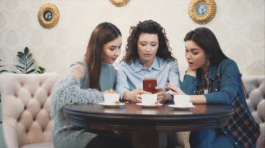 Bir kafede akıllı telefonla oturan ve komik bir konuşma olan üç arkadaş. Uzun güzel siyah saçlı iyi kızlar. Masada üç bardak kapuçino.