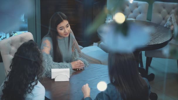 Drie jonge mooie meiden zitten in een café. Tijdens deze vriendin communiceren. Hebben mooie zwarte lange haren. Na een lange scheiding. — Stockvideo