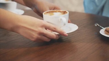 Kafede masada büyük plan kapuçino fincan. Bu kız sırasında, bir yudum kapuçino zevk olan kahverengi masaya bir fincan koyar.