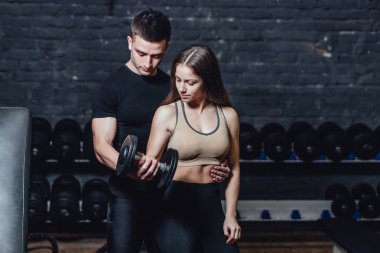 Bir spor kadını kaslı bir egzersiz yapıyor. Kırmızı bir arka plan üzerinde dumbbells ile Fotoğraf kas fitness modeli geliştirme. Güç ve motivasyon.
