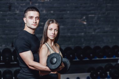 Two young guys and girls are engaged in the gym. During this time, they embraced themselves holding their weights in their hands. clipart