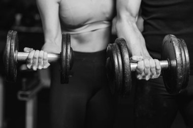 Fitness, spor, egzersiz ve halter. Konsept - genç bir kadın ve dambılı genç bir adam spor salonunda kaslarını temizliyor..