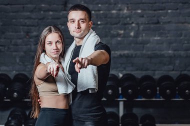 Genç sportif çift adam ve kız spor salonunda ayakta. Bu esnada, beyaz pislik boynunda tutulur. Siyah bir arka plan üzerinde durup kameraya bakmak.