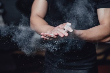 Güzel yakışıklı genç atlet siyah t-shirt giymiş. Bu süre zarfında, lastiklerin üzerinde oturan ve spor salonunda ellerinize talk uygulayarak.