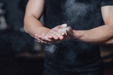 Güzel yakışıklı genç atlet siyah t-shirt giymiş. Bu süre zarfında, lastiklerin üzerinde oturan ve spor salonunda ellerinize talk uygulayarak.