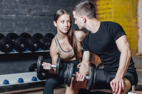 Fitness, sports, exercices et haltérophilie. Concept - une jeune femme et un jeune homme avec des haltères balayant les muscles dans la salle de gym. Pendant ce temps, ils regardent leurs muscles . — Photo