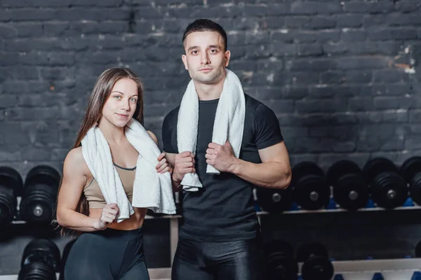 Jeune couple sportif homme et fille debout dans la salle de gym. Pendant ce temps, l'ordure blanche est maintenue sur le cou . — Photo