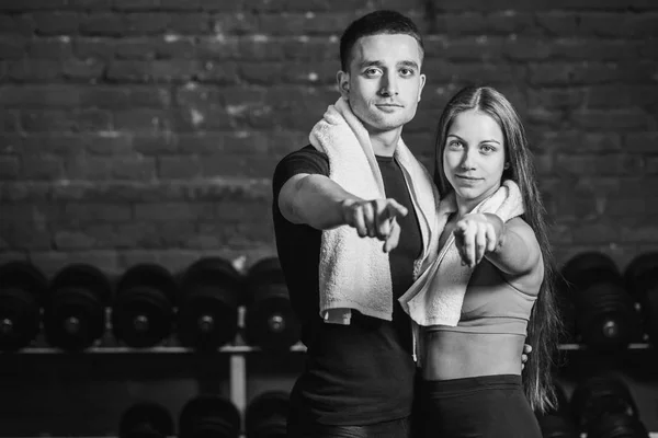 Jeune couple sportif homme et fille debout dans la salle de gym. Pendant ce temps, l'ordure blanche est maintenue sur le cou. Debout sur un fond noir et en se regardant. Noir et blanc . — Photo