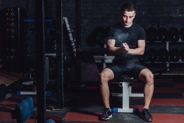 Güzel yakışıklı genç atlet siyah t-shirt giymiş. Bu süre zarfında, lastiklerin üzerinde oturan ve spor salonunda ellerinize talk uygulayarak.