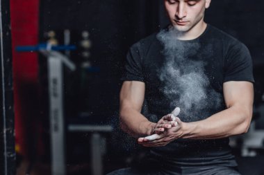 Güzel yakışıklı genç atlet siyah t-shirt giymiş. Bu süre zarfında, lastiklerin üzerinde oturan ve spor salonunda ellerinize talk uygulayarak.
