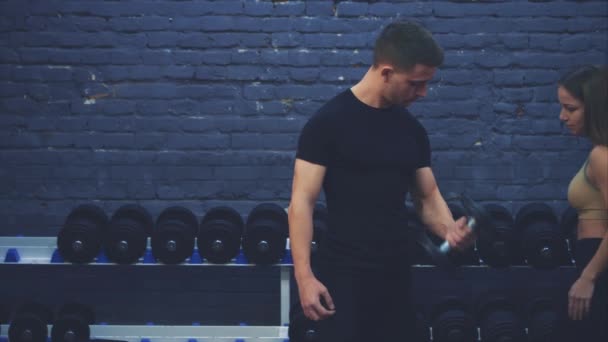 Un jeune garçon en T-shirt noir. Un grand haltère dans la salle de gym entraîne régulièrement les mains sur un fond sombre . — Video