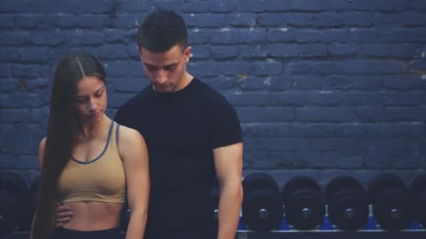 Une belle jeune fille et son petit ami bien construit montrent ensemble un cours de geste. Ils sont heureux de se voir dans la salle de gym . — Video