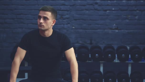 Joven deportista con ropa deportiva en el gimnasio. Tensionando durante una sesión de entrenamiento, me fui a descansar. Vestido con una camiseta negra . — Vídeos de Stock