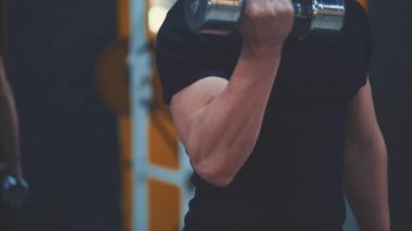 Spor salonunda genç güzellik eğitmeni. Bu süre zarfında, atlet düzenli dumbbells ile eğitim yapar. Siyah bir t-shirt giymiş.