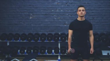 Siyah tişört giyen sportif genç adam. Spor vücutlu bir adam sınıf gösterir. Bu esnada, diğer taraftan ağırlığı tutar.