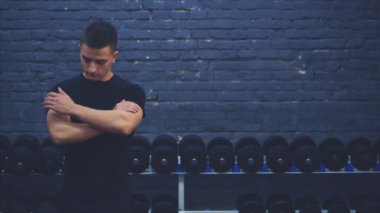 Siyah tişört giyen sportif genç adam. Sportif vücutlu bir adam elini uzatır. Bu süre zarfında kaslarını gösterir. Bu süre zarfında spor salonunda..