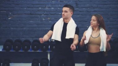 Spor salonunda bir kızla siyah bir tişört giyen spor genç bir çocuk. Spor organları olan insanlar. Bu süre zarfında parmaklarını farklı yönlere sallıyorlar. Spor salonundalar..