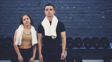 Spor salonunda bir kızla siyah bir tişört giyen spor genç bir çocuk. Spor organları olan insanlar. Bu esnada, elleri bir çağrı jesti göstererek el sallarlar. Spor salonundalar..