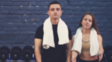 Spor salonunda bir kızla siyah bir tişört giyen spor genç bir çocuk. Spor organları olan insanlar. Bu esnada, elleri bir çağrı jesti göstererek el sallarlar. Spor salonundalar. Bulanık