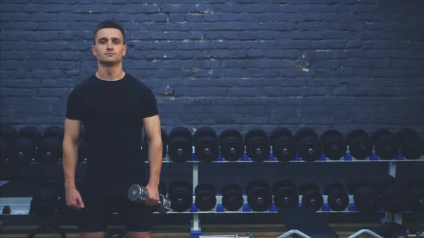 Un joven deportivo con una camiseta negra. Un hombre con un cuerpo deportivo muestra una clase. Durante esto, sostiene el peso en la otra mano . — Vídeos de Stock