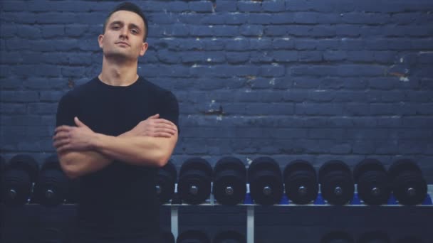 Sporty young guy wearing a black T-shirt. A man with a sporty body puts a hand on his hand. During this time it shows its muscles. During this time he is in the gym. — Stock Video