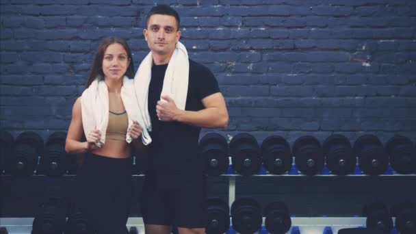 Spor salonunda bir kızla siyah bir tişört giyen spor genç bir çocuk. Spor organları olan insanlar. Bu esnada, kız elini koluna koyar. Spor salonundalar.. — Stok video