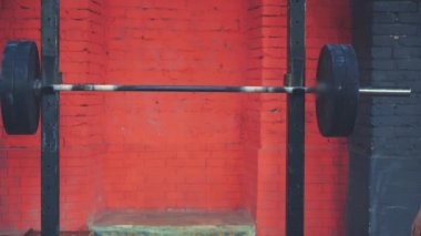 Binici omuzlarında çok ağır bir çubuk ile duruyor. O üst ve bir bar yerleştirir. Siyah tişört giymiş genç bir sporcu, spor salonunu tanıyın..