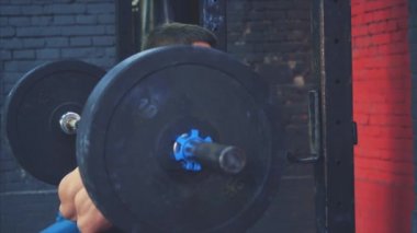 Binici omuzlarında çok ağır bir çubuk ile duruyor. O üst ve bir bar yerleştirir. Siyah tişört giymiş genç bir sporcu, spor salonunu tanıyın. Kırmızı arka plan.