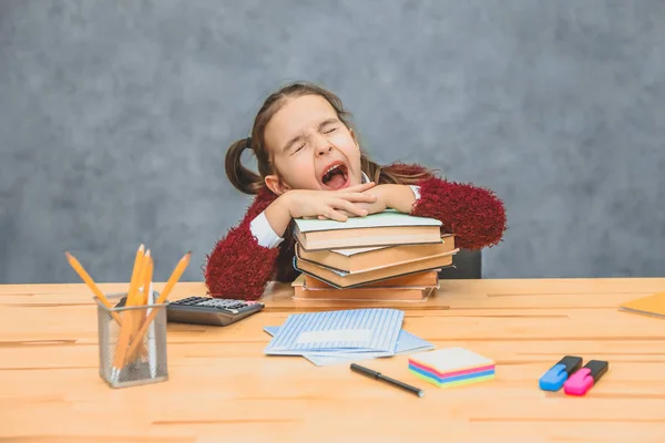 Ganska ganska Schoolgirl flicka sitter vid bordet. Under detta, hålla huvudet på de böcker som står på bordet. Slutna ögon dansen öppnade hennes mun gäspningar. — Stockfoto