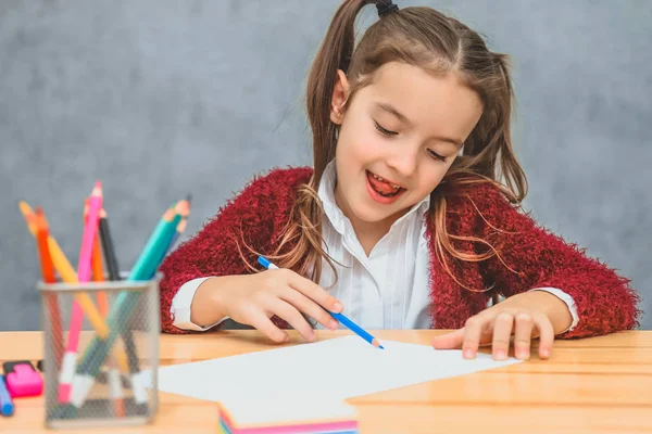 Hermosa chica sobre fondo gris. Tomar un lápiz azul disfruta del proceso de dibujo. En la mesa hay lápices de color rosa . — Foto de Stock