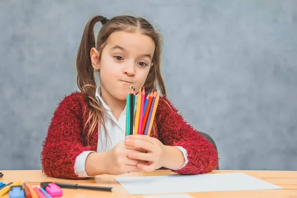 Крупный план цветных карандашей в одной руке девочек. Серый фон. Марионетка смотрит на карандаши. Одетый в красную куртку . — стоковое фото