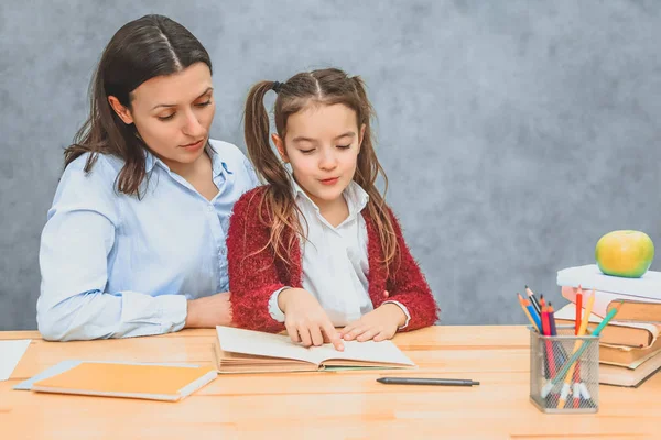 Mother and daughter read a book on a gray background, doing homework. Dressed in beautiful shirts. — Stock Photo, Image