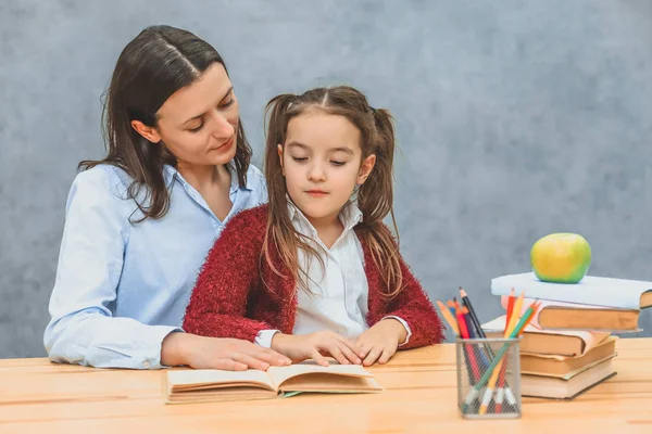 Jovem mãe e filha sentadas em uma mesa lendo um livro. Durante este olhar no livro. Emoções sinceras . — Fotografia de Stock