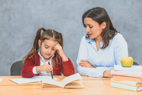 Mamma hjälper mig att göra mina döttrar läxor. Under detta sitter de på en grå bakgrund. — Stockfoto